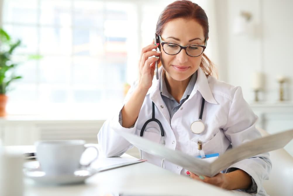 A focused female physician talking on the phone while reading