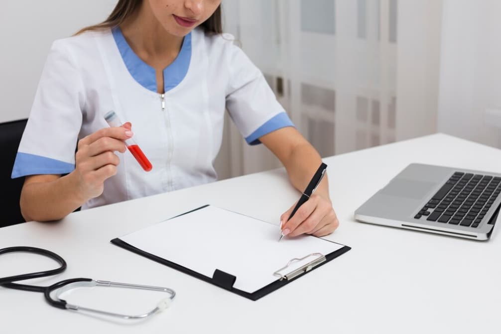 A healthcare professional is analyzing a blood sample next to a laptop